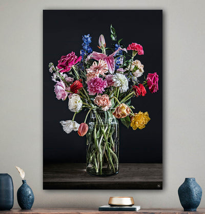 Schilderij met kleurrijke bloemen in een glazen vaas tegen een beige muur