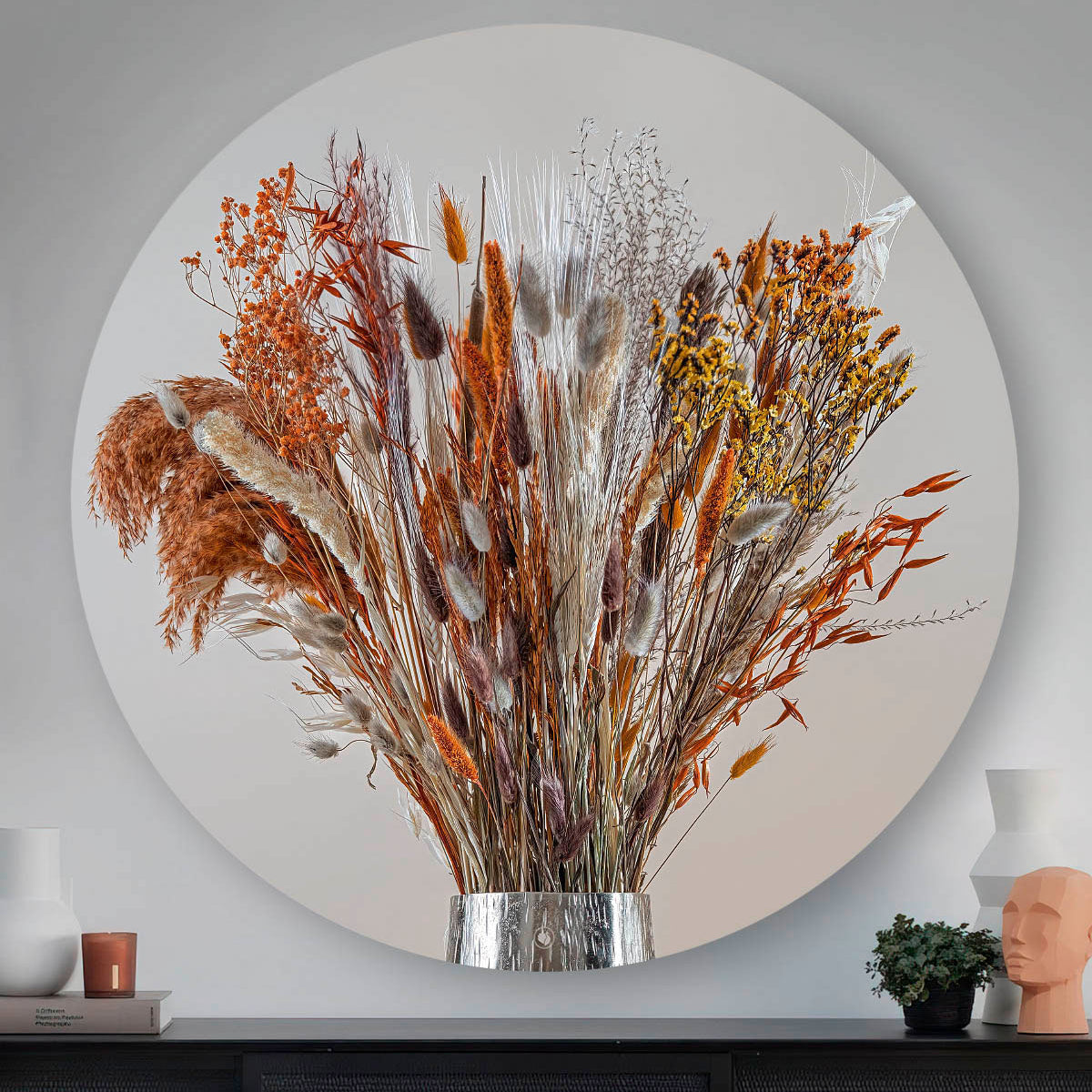 Wandcirkel met droogbloemen met koper kleur tegen een muur en boven een zwart dressoir