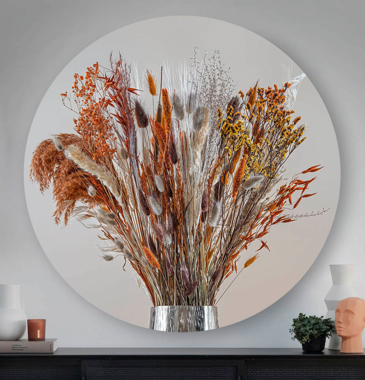 Wandcirkel met droogbloemen met koper kleur tegen een muur en boven een zwart dressoir