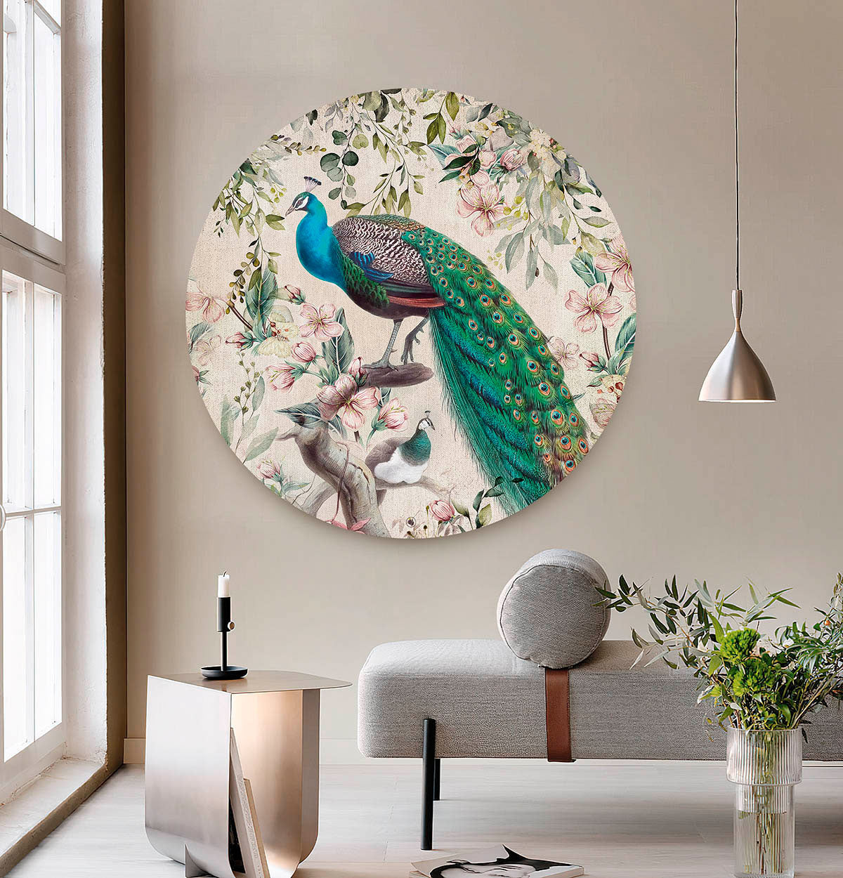 Muurcirkel met pauwen met een groene staart en roze bloemen tegen een beige muur en een grijze bank
