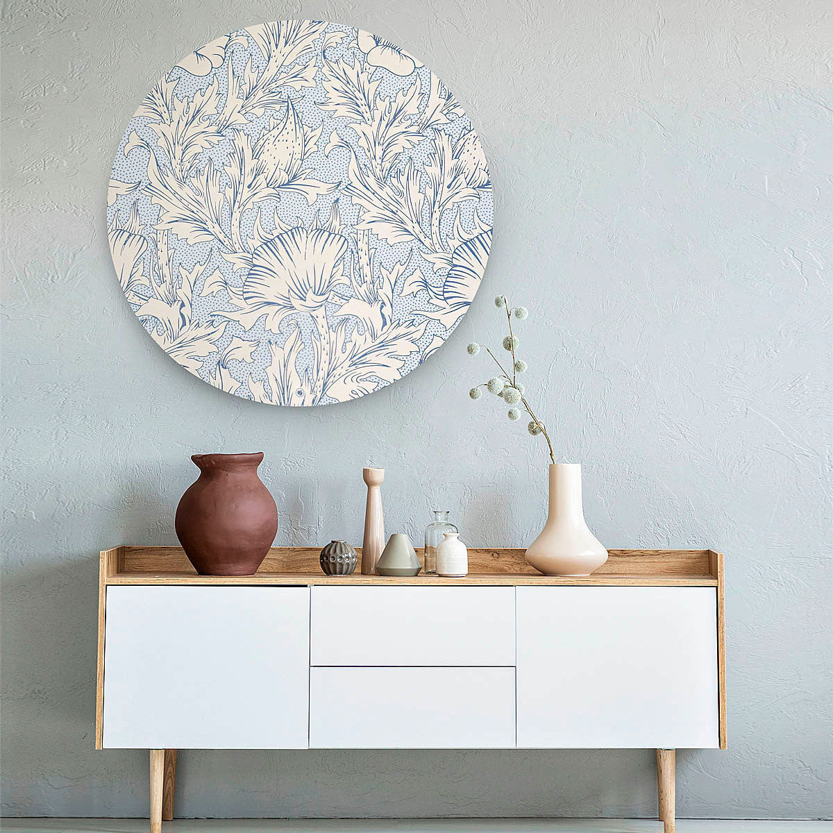 Muurcirkel met blauw bloemenpatroon tegen een licht blauwe muur met een wit dressoir en vazen