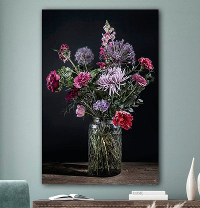 Schilderij met kleurrijke bloemen in een glazen vaas tegen een zacht groenemuur