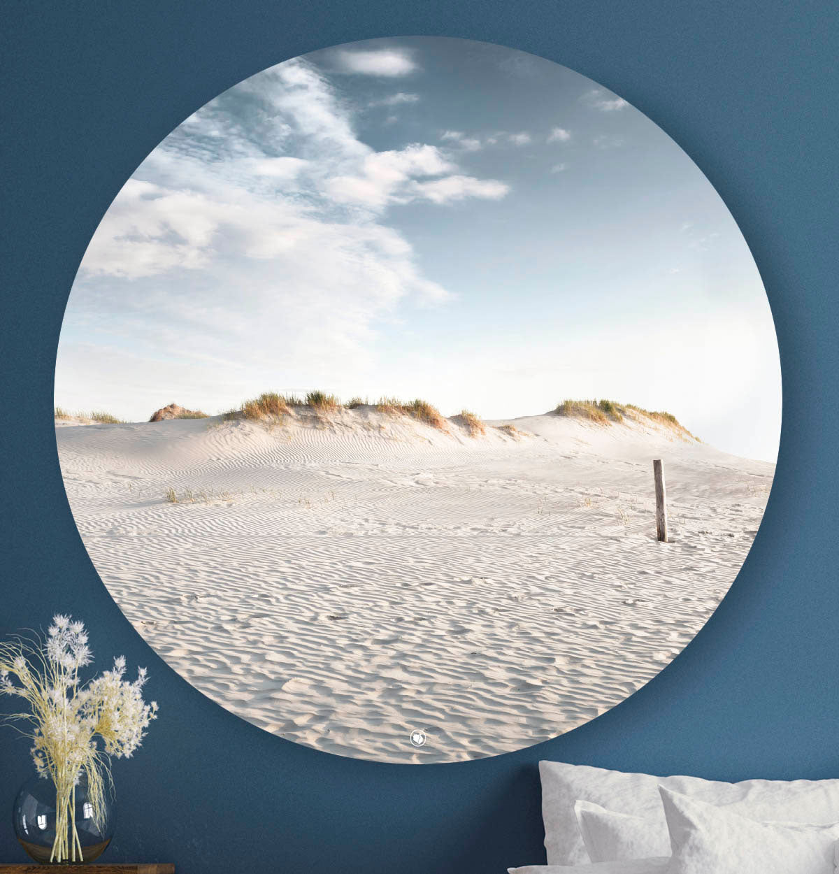 Wandcirkel met strand, duinen en blauwe lucht erop tegen een blauwe muur