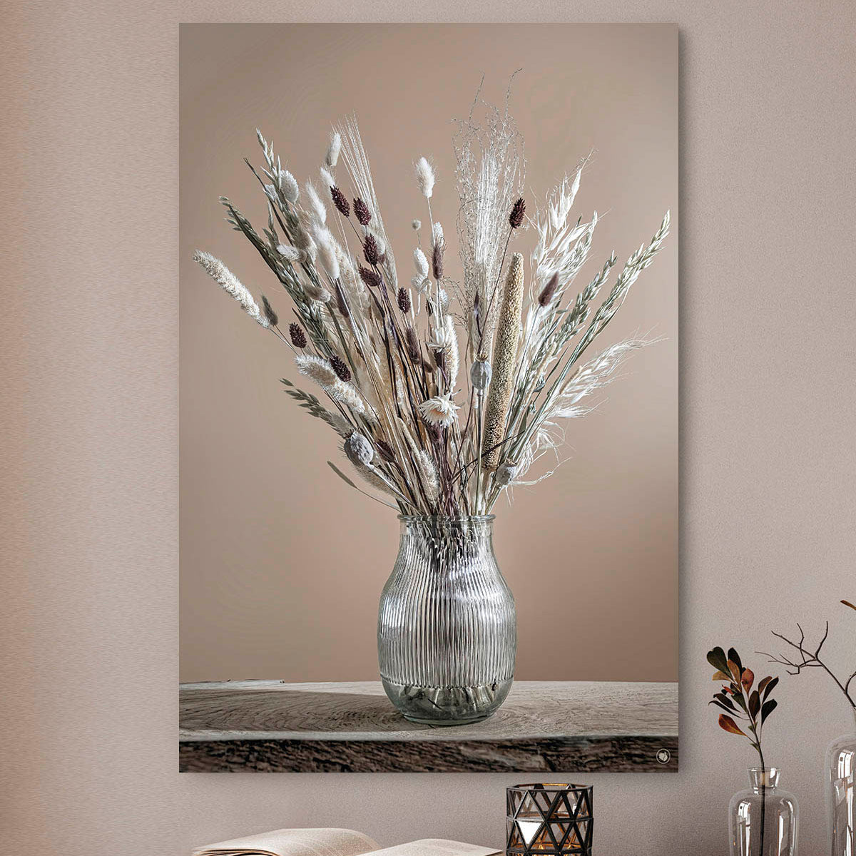 Wanddecoratie met witte en bruine droogbloemen in een glazen vaas tegen een beige muur